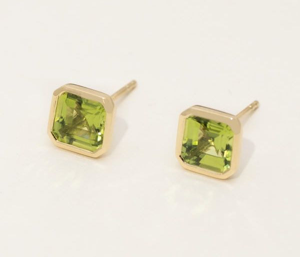 Gold earrings with green gemstones on a white background