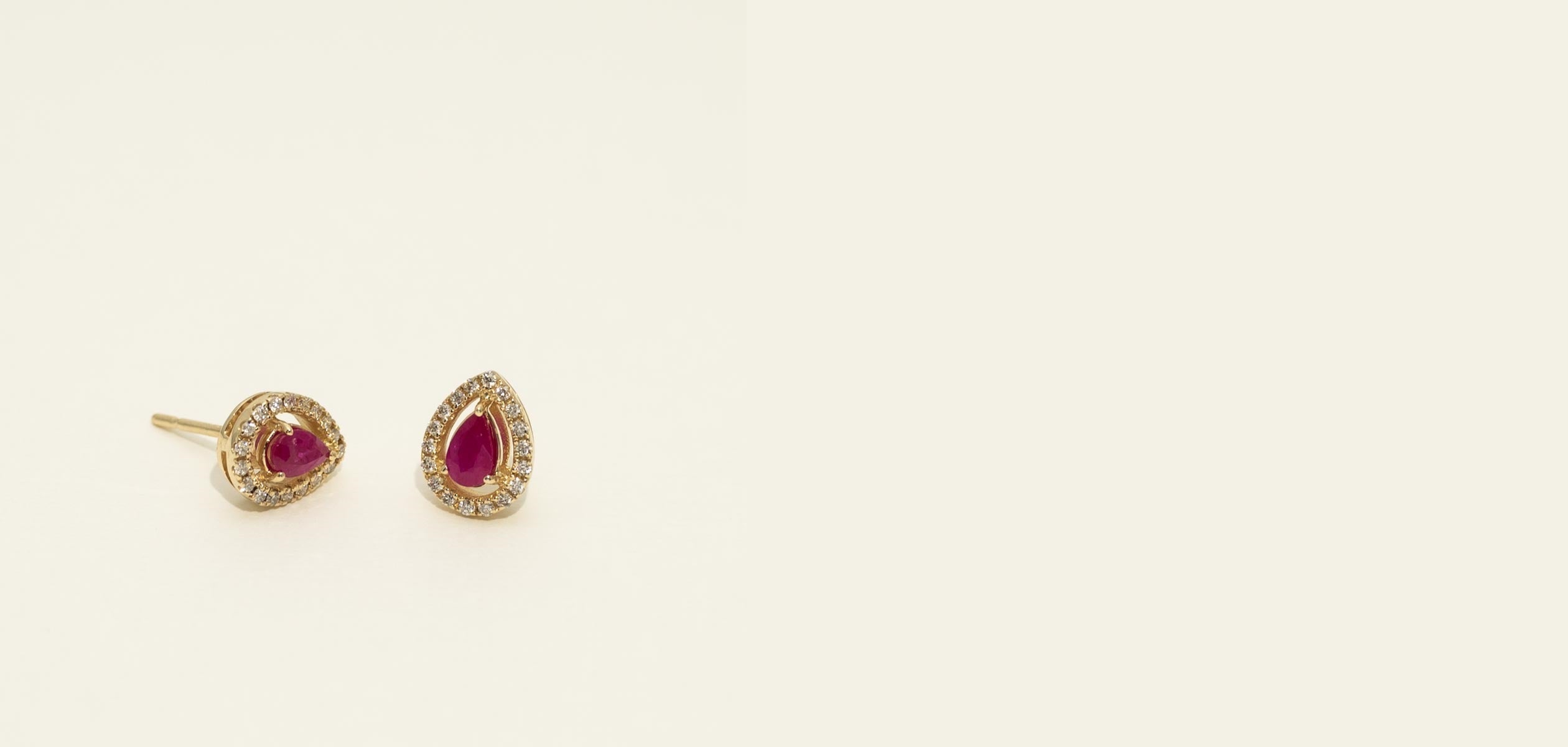Pair of gold earrings with red gemstones on a beige background