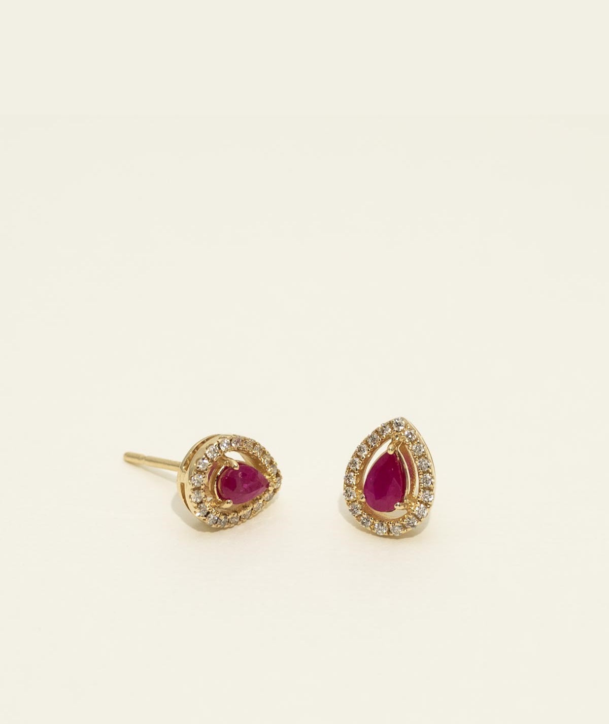 Pair of gold earrings with red gemstones on a beige background