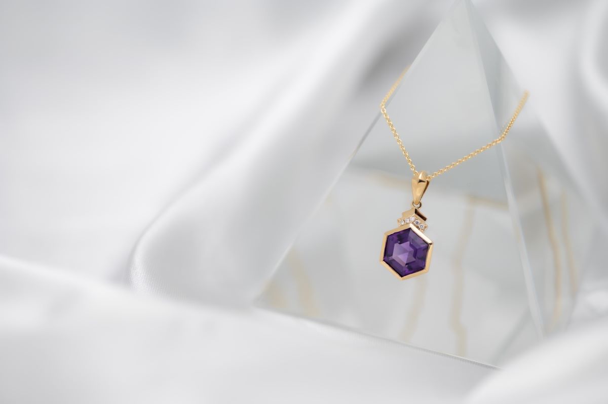 purple hexagonal stone set in a yellow gold necklace