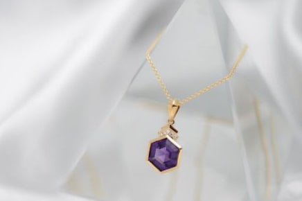 Gold necklace with a purple pendant on a white fabric background