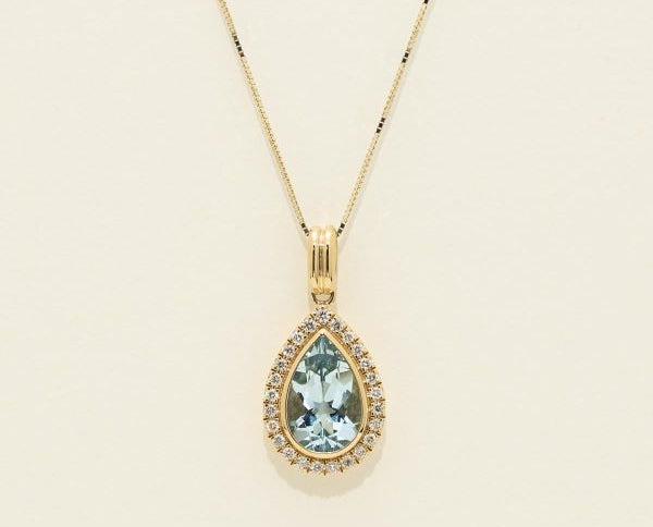 Gold necklace with a teardrop-shaped gemstone pendant on a beige background