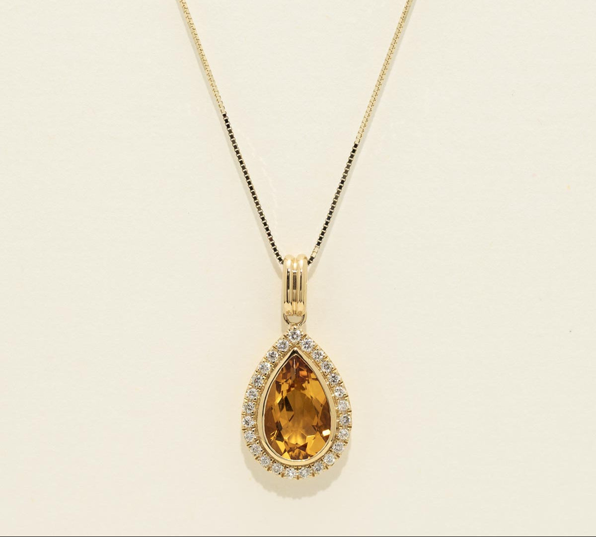 Gold necklace with a teardrop-shaped yellow gemstone pendant on a beige background