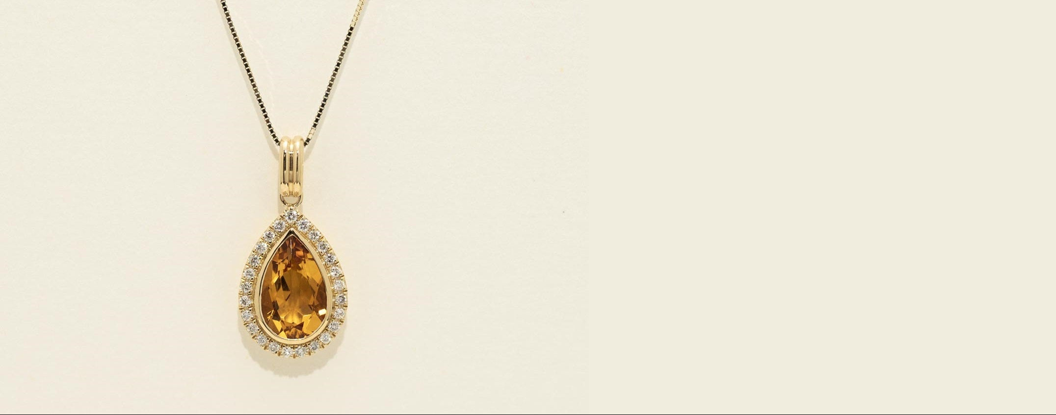 Gold necklace with a teardrop-shaped citrine pendant on a beige background
