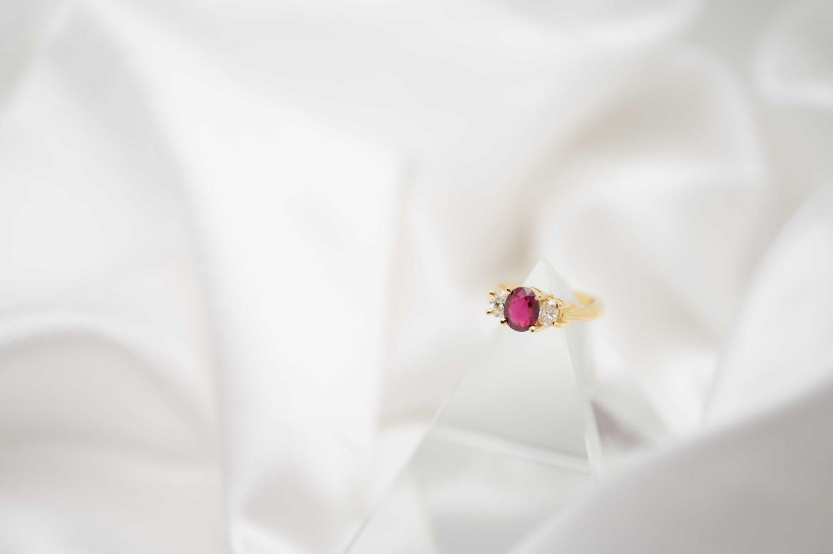 Gold ring with a red gemstone on a white fabric background