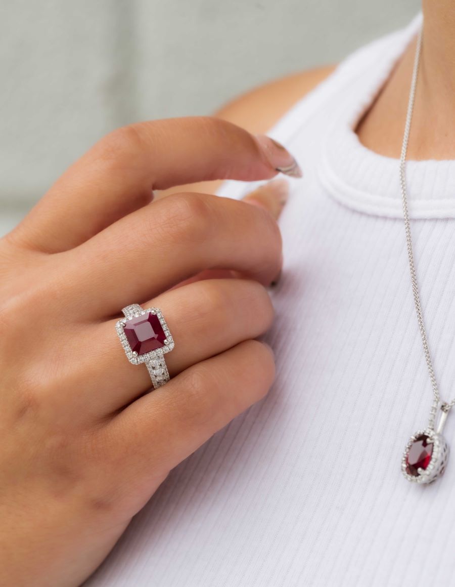 Close-up of a hand wearing a red gemstone ring with a matching pendant on a plain background