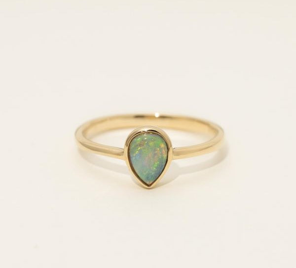 Gold ring with a teardrop-shaped opal stone on a light beige background