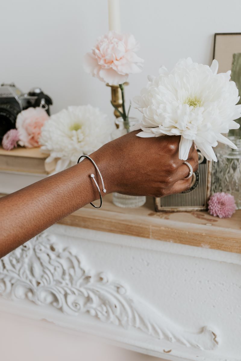 Person holding a white flower in a decorative setting with candles and flowers.