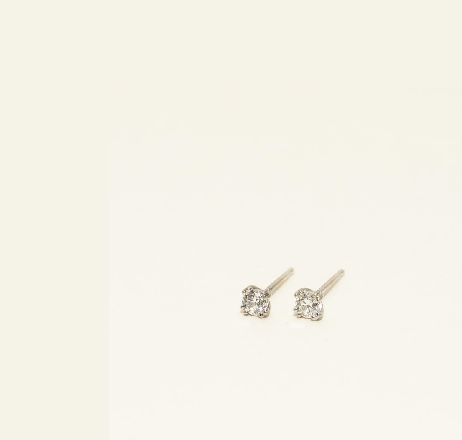 Pair of diamond stud earrings on a light beige background