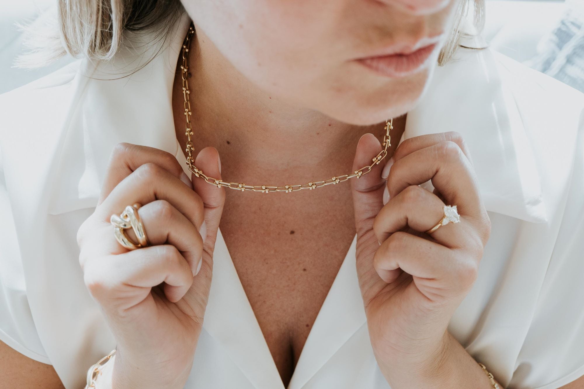 Person wearing a gold necklace with a close-up of hands adjusting it.