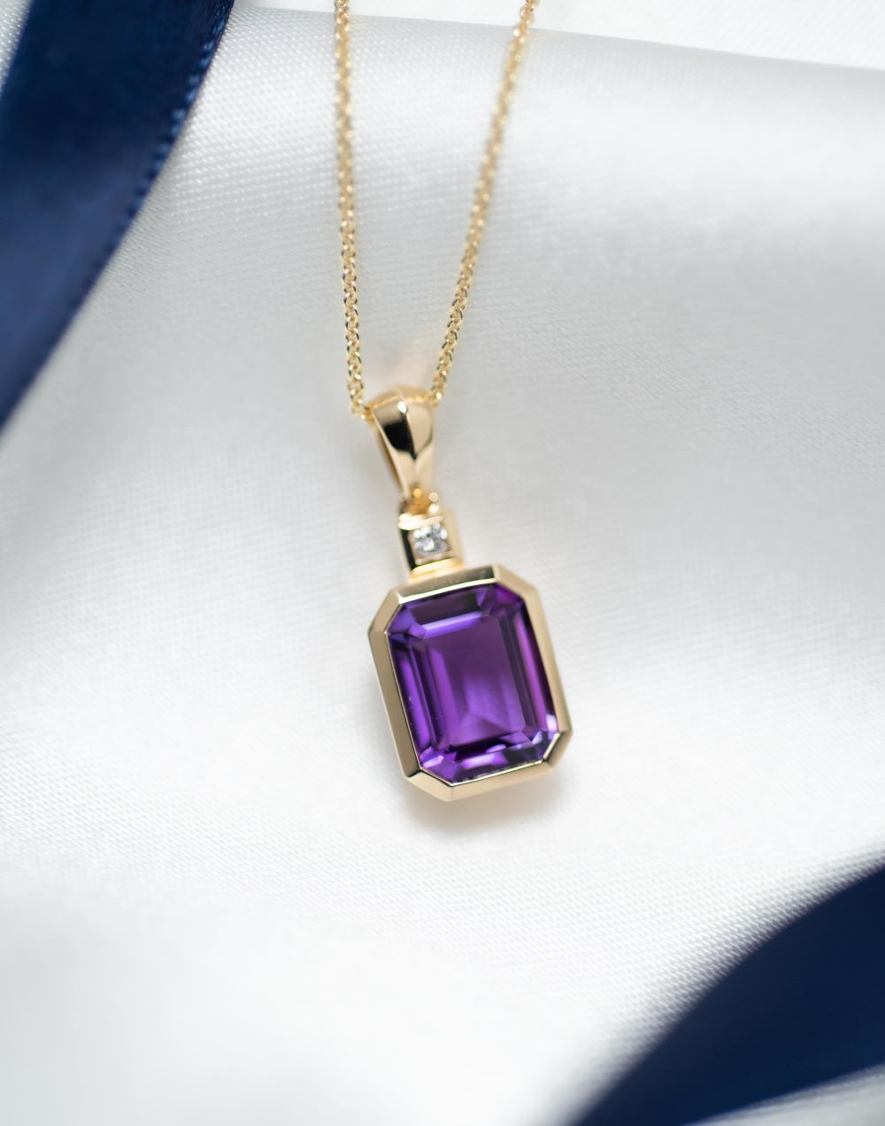 Gold necklace with a purple gemstone pendant on a white background