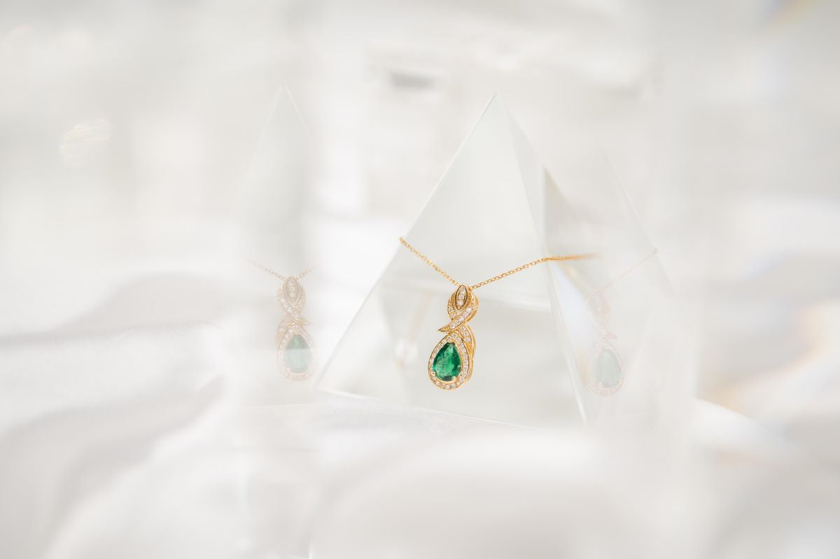 Gold necklace with a green gemstone pendant on a white background