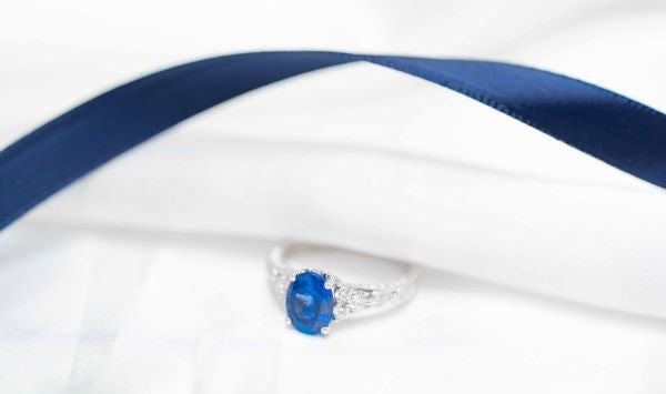 Silver ring with a blue gemstone on a white and blue satin background