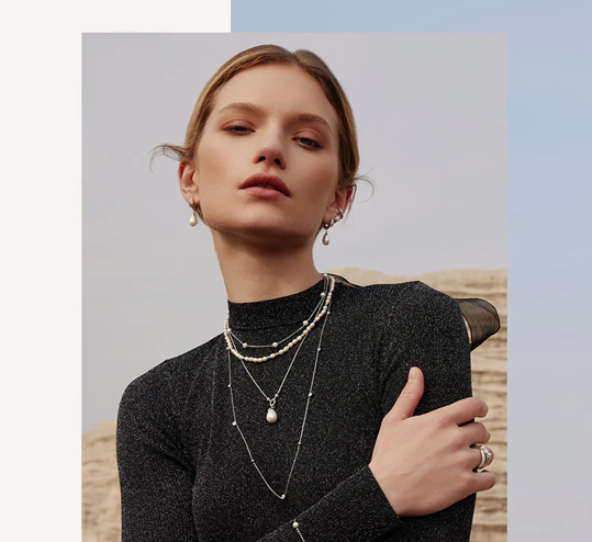 Woman wearing layered necklaces and a ring, with a neutral background