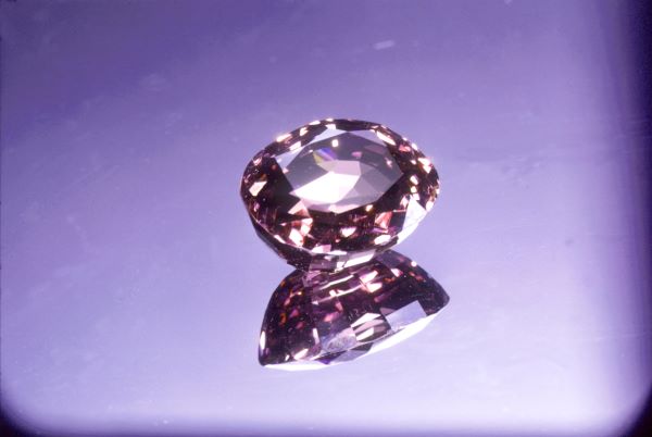 Pink gemstone with a reflective surface on a purple background