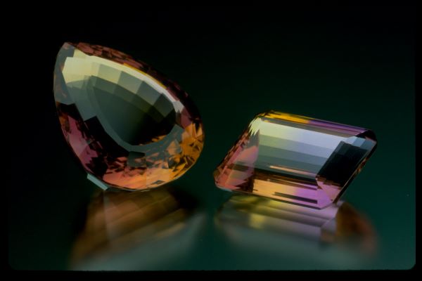 Two multicolored gemstones on a reflective surface with a dark background